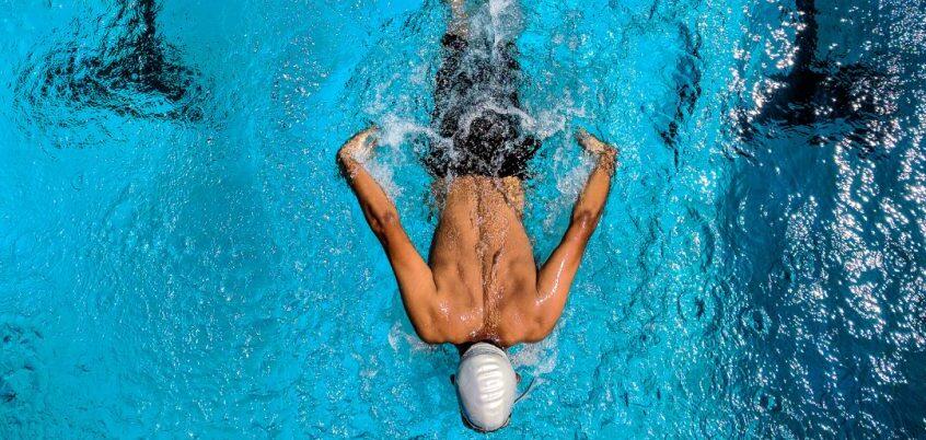 Schwimmer in der Wasserlage mit angespannten Armen und Schwimmkappe, schwimmt im klaren blauen Wasser eines Schwimmbeckens.