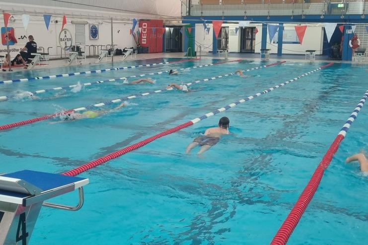 Schwimmer in einem Indoor-Pool während des Trainings, mit Wasser, Rettungsgeräten und Ausrüstungsgegenständen am Beckenrand.