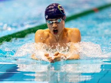 Junger Schwimmer beim Brustschwimmen im Pool, Wasser spritzt um ihn herum.