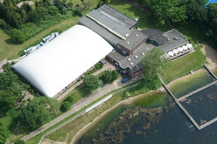 Luftaufnahme eines Gebäudes neben einem See, mit Garten, Steg und Booten am Ufer.