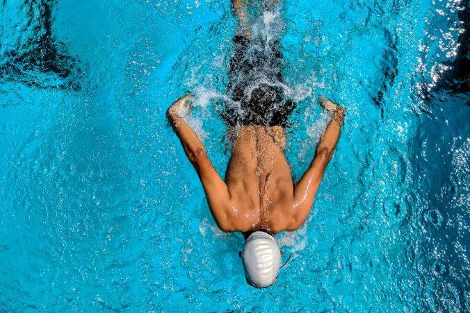 Schwimmer in der Wasserlage mit angespannten Armen und Schwimmkappe, schwimmt im klaren blauen Wasser eines Schwimmbeckens.