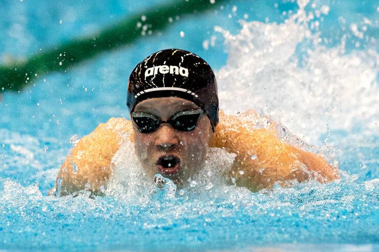 Schwimmer in schwarzer Badekappe und Sonnenbrille, der energetisch im Wasser schwimmt, mit Spritzern um ihn herum.