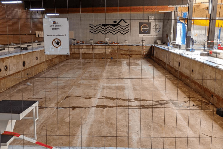 Leeres Schwimmbecken mit Absperrgitter und Hinweisschild "25m-Becken gesperrt" in einem Schwimmbad.