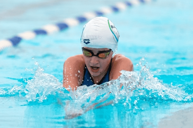 Schwimmerin mit Badekappe und Brille vollbringt eine Brustschwimmtechnik im blauen Wasser eines Schwimmbeckens.