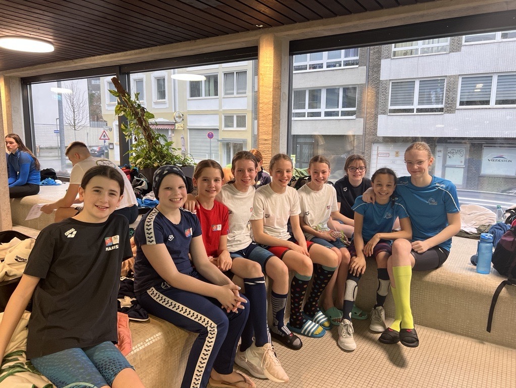 Gruppenfoto von acht Mädchen in Sportkleidung, die auf einem Sitzbereich in einem hellen Raum posieren.