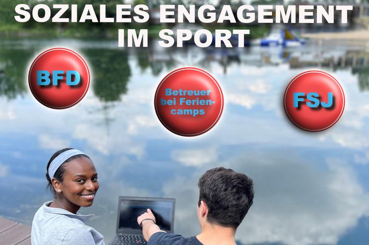 Zwei Personen sitzen am Ufer eines Sees, eine zeigt auf einen Laptop, während die andere lächelt.