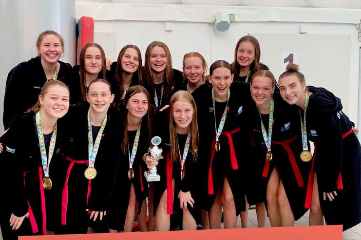 Gruppe von zehn jungen Frauen in Schwimmbekleidung, die stolz einen Pokal und Medaillen präsentieren.