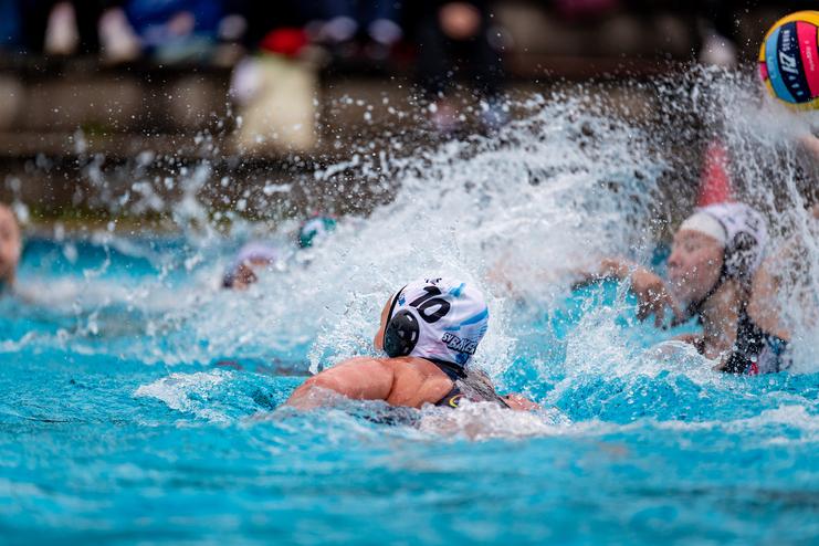 Wassersport-Szene mit schwimmender Spielerin im blauen Wasser, umgeben von Spritzwasser und weiteren Athletinnen.