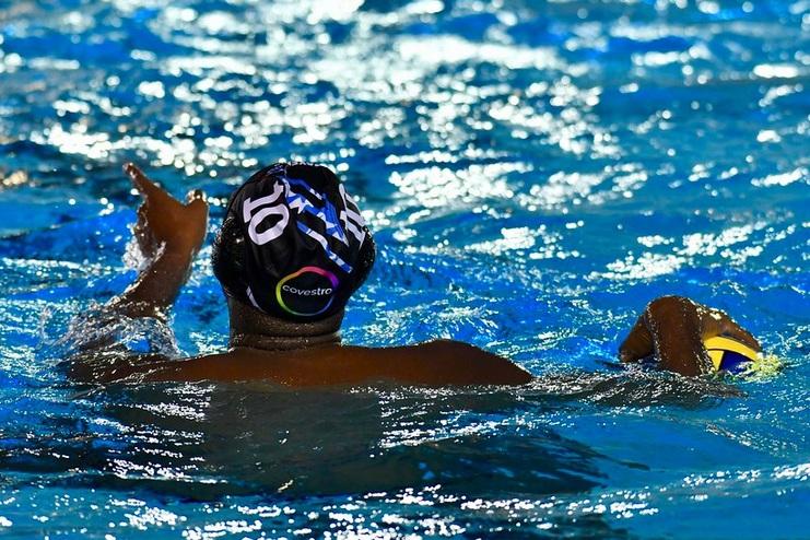 Wasserspieler in einem Pool hebt die Hand, während er einen Wasserball mit der anderen Hand hält.