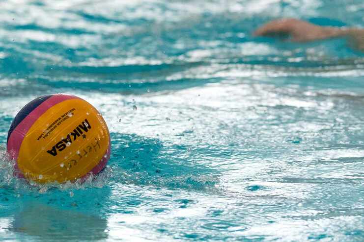 Wasserball rollt auf der Oberfläche eines Schwimmbeckens, umgeben von spritzendem Wasser.