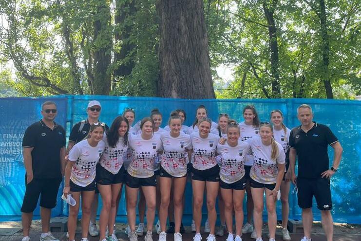 Gruppe von zwölf Frauen in Sportbekleidung, Posieren vor einem blauen Banner und großen Bäumen im Hintergrund.