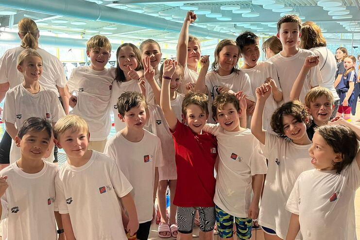 Gruppe von Kinder-Schwimmern in weißen T-Shirts, posierend mit sportlicher Begeisterung am Schwimmbecken.