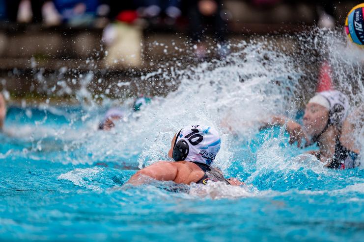 Wassersport-Szene mit schwimmender Spielerin im blauen Wasser, umgeben von Spritzwasser und weiteren Athletinnen.