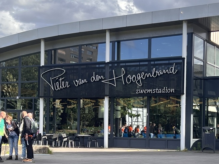Eingang des Pieter van den Hoogenband Schwimmstadions mit mehreren Personen im Freien.
