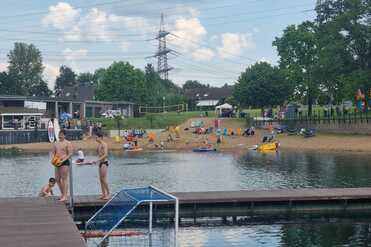 Zwei Jungen mit Wassertropfen stehen am Steg, während im Hintergrund Strandbesucher am Wasser entspannen.