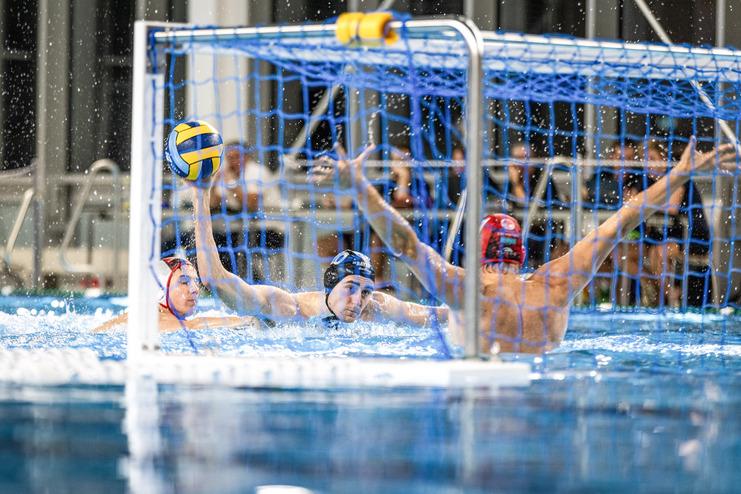 Wasserballspieler in Aktion: Ein Spieler wirft den Ball durch das Tor-Netz, w&auml;hrend Wasser spritzt.