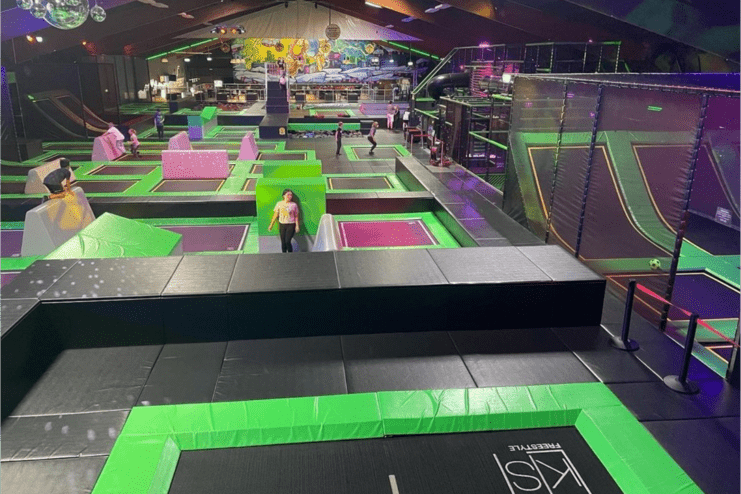 Trampolinpark mit verschiedenen Sprungfl&auml;chen und Hindernissen, viele Personen in aktiver Bewegung im Innenraum.