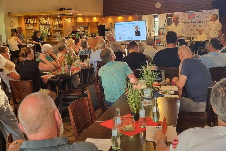 Versammlung in einem Restaurant mit zahlreichen Teilnehmern, Drinks auf den Tischen und Präsentation an der Wand.