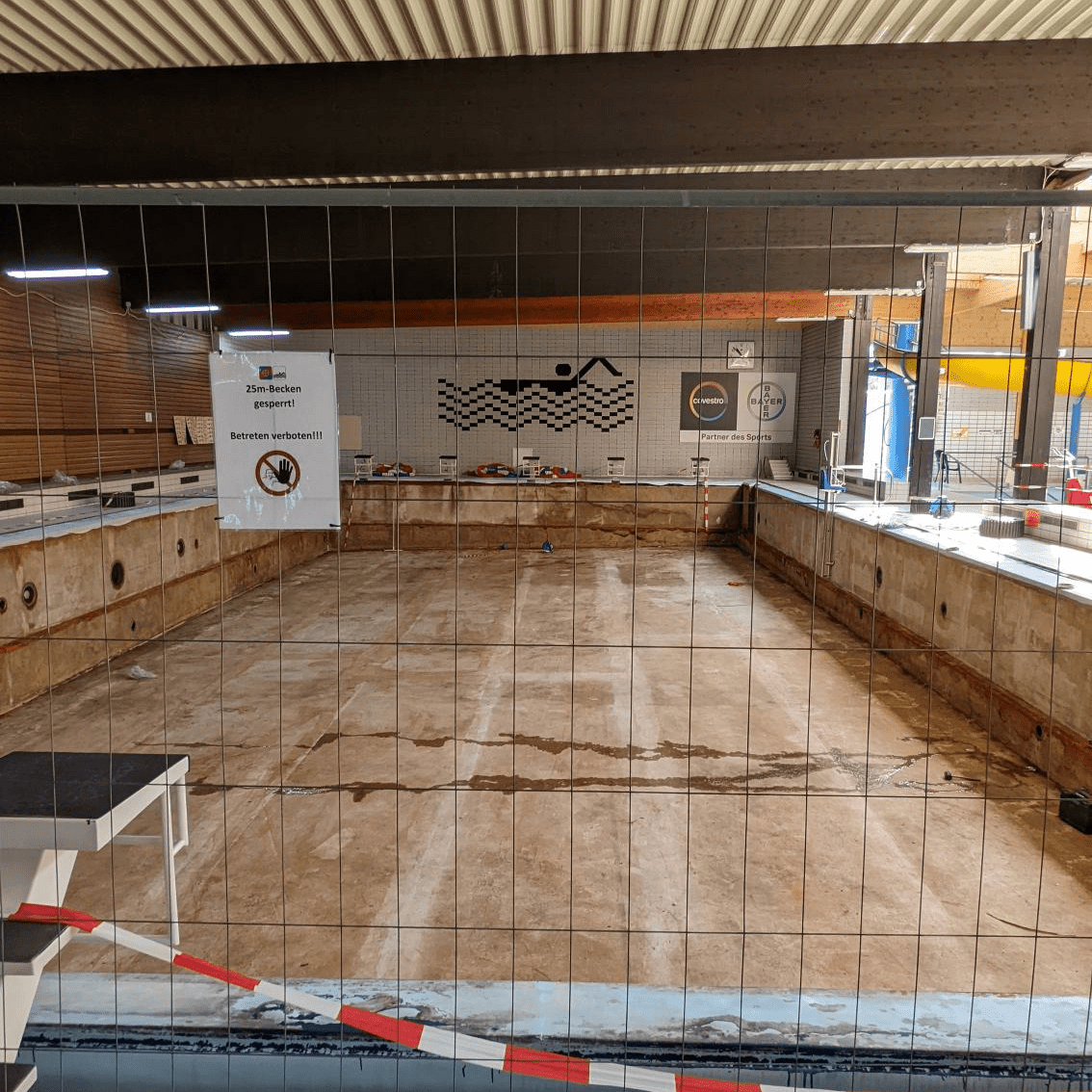 Leeres Schwimmbecken mit Absperrgitter und Hinweisschild "25m-Becken gesperrt" in einem Schwimmbad.