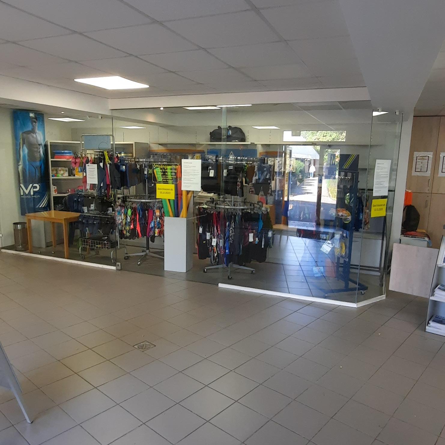 Innenansicht eines Gesch&auml;fts mit Regalen voller Kleidung und einem Glas-Eingang, gut beleuchtet und ger&auml;umig.