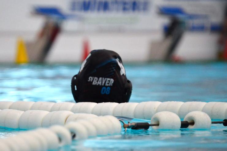 Wassersporthelm mit der Aufschrift "SV Bayer 08" vor einer Schwimmbahn in klarem Wasser.
