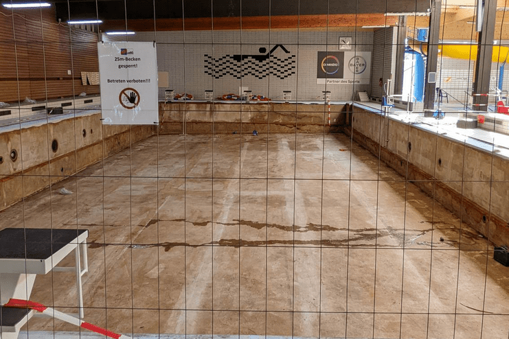 Leeres Schwimmbecken mit Absperrgitter und Hinweisschild "25m-Becken gesperrt" in einem Schwimmbad.