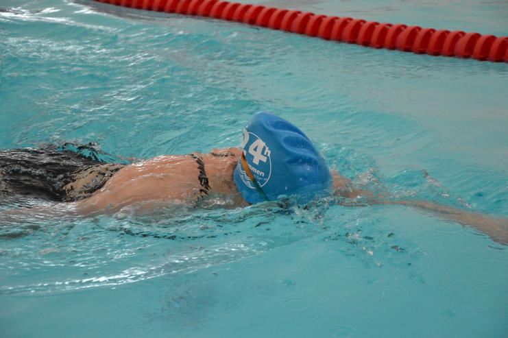 Schwimmer mit blauer badekappe schwimmt in einem Hallenbad, Wasser spritzt um das Gesicht und den Körper.