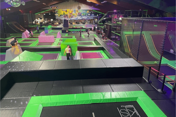 Trampolinpark mit verschiedenen Sprungflächen und Hindernissen, viele Personen in aktiver Bewegung im Innenraum.