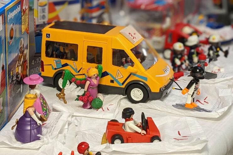 Bunte Playmobil-Szene mit gelbem Fahrzeug, Figuren mit Blumen und Sportgeräte auf einem Tisch.