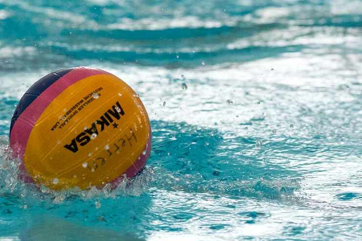 Wasserball rollt auf der Oberfläche eines Schwimmbeckens, umgeben von spritzendem Wasser.