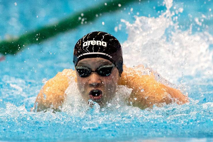 Schwimmer in schwarzer Badekappe und Sonnenbrille, der energetisch im Wasser schwimmt, mit Spritzern um ihn herum.