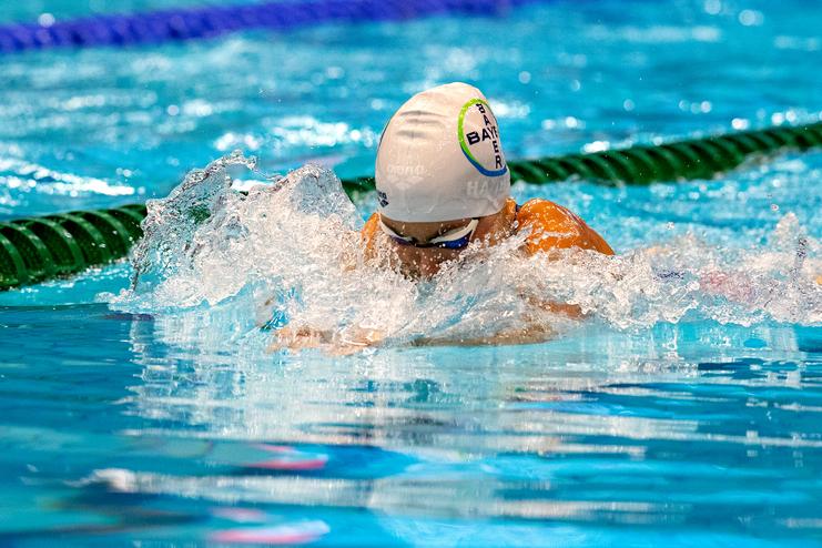 Schwimmerin im Wasser mit weißer Badekappe, die einen Schwimmstil ausführt und Wasser spritzt.