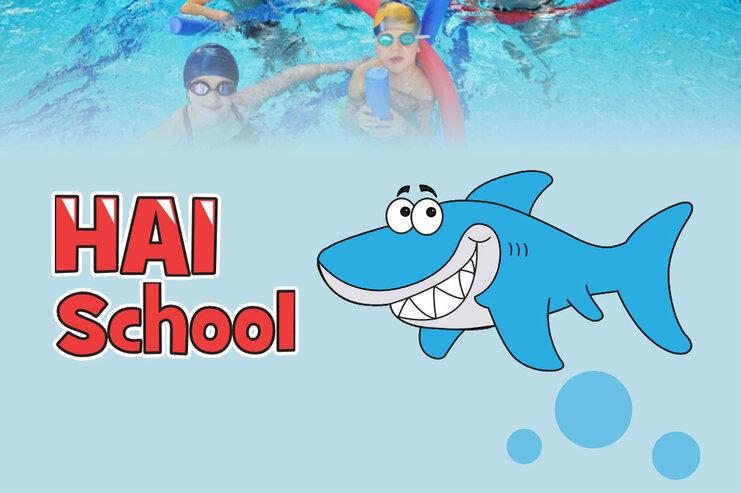 Gruppe von Kindern mit Schwimmbrillen im Wasser, umgeben von Schwimmnudeln, neben dem Schriftzug „HAI School“.