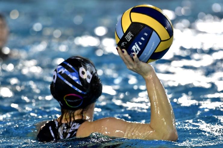 Wasserballspielerin hält einen gelben und blauen Ball über dem Wasser in einem Schwimmbad.
