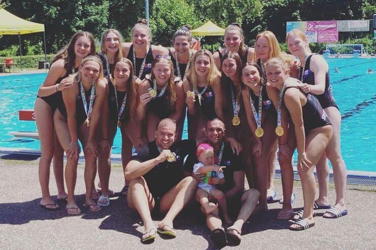 Gruppe von 15 Frauen in Sportkleidung mit Medaillen, umgeben von einem Schwimmbecken an einem sonnigen Tag.