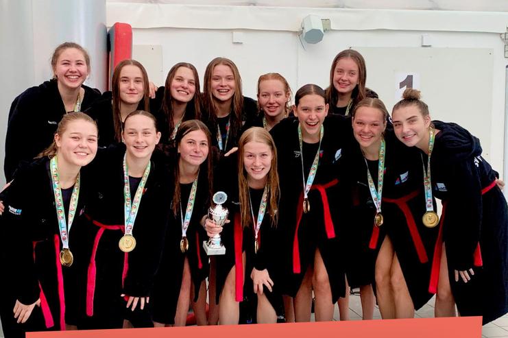 Gruppe von zehn jungen Frauen in Schwimmbekleidung, die stolz einen Pokal und Medaillen pr&auml;sentieren.