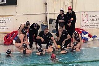 Trainingssituation im Wasserball mit Trainer und zehn Spielerinnen in einem Schwimmbecken, Taktikbesprechung in Aktion.