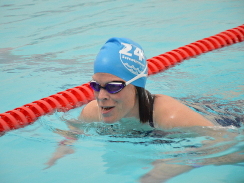 Schwimmerin mit blauer Badekappe und Schwimmbrille im Wasser, lächelnd, vor rotem Bahnmarkierungsband.