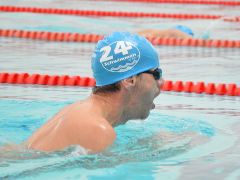 Schwimmer im blauen Badekappe bei einem Wettkampf im Wasser, mit roter Abgrenzung im Hintergrund.