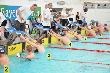 Schwimmer bereit an den Startblöcken in einem Wettkampfbecken, während Betreuer die Zeit stoppen.