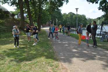 Menschen entspannen in einem Park, einige spielen, andere unterhalten sich am Ufer eines Gewässers.