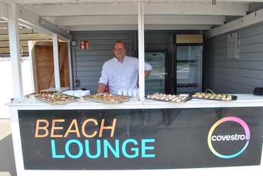 Mann in Kochjacke steht an einer Beach Lounge mit verschiedenen Tänken und einem Schilder mit der Aufschrift „BEACH LOUNGE“.