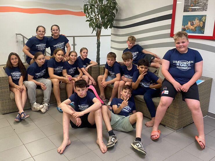 Gruppe von Jugendlichen in blauen T-Shirts sitzt auf einem Sofa in einem Fitnessbereich, umgeben von einer modernen Wandgestaltung.