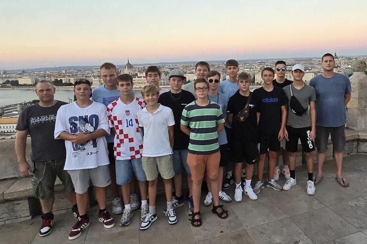 Gruppe von Jugendlichen und Erwachsenen posiert vor Aussichtspunkt mit Blick auf Stadtlandschaft und Fluss bei Sonnenuntergang.