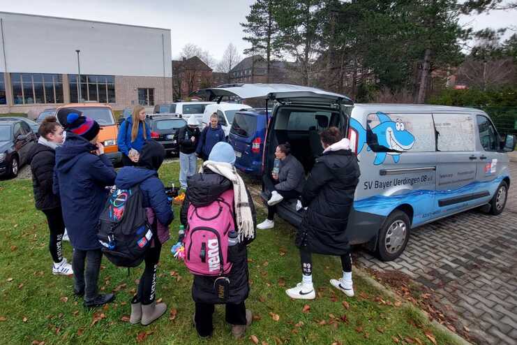 Gruppe von Kindern und Jugendlichen versammelt sich um einen Verkaufswagen auf einem Parkplatz neben einem Gebäude.