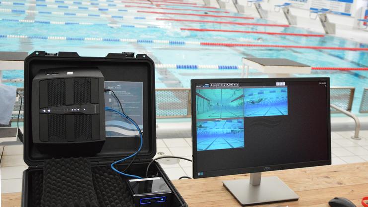 Technik zur Analyse von Schwimmtechniken auf einem Tisch in einem Schwimmbad mit Blick auf das Wasser und die Bahnen.