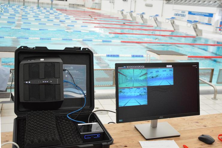 Technik zur Analyse von Schwimmtechniken auf einem Tisch in einem Schwimmbad mit Blick auf das Wasser und die Bahnen.