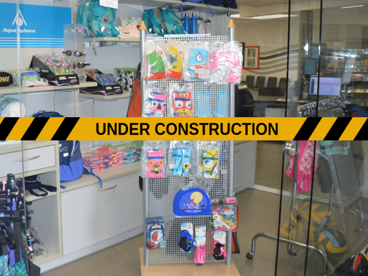 Laden mit Schwimmausrüstung und Rucksäcken, überlagert von einem „UNDER CONSTRUCTION“-Schild.