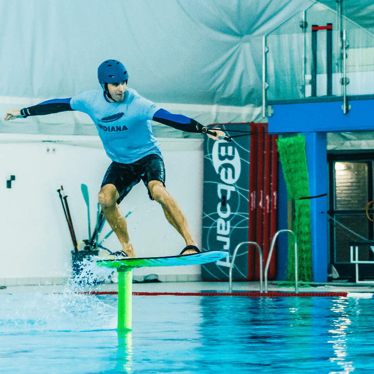 Surfer auf einem Foilboard schwebt über einer grünen Boje in einem Hallenbad, Wassertropfen spritzen auf.
