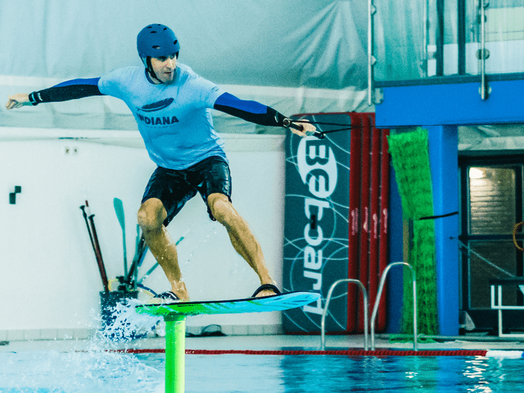 Surfer auf einem Foilboard schwebt über einer grünen Boje in einem Hallenbad, Wassertropfen spritzen auf.